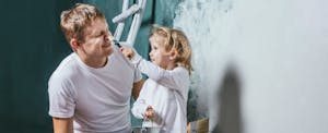 Dad painting a room with his daughter and explaining to her how to get a great mortgage rate