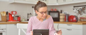 Woman sitting in her kitchen, looking at her credit card,
