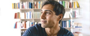 Smiling young man in front of his bookshelves at home