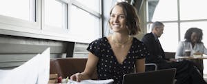 Smiling, confident businesswoman with paperwork using laptop in airport lounge