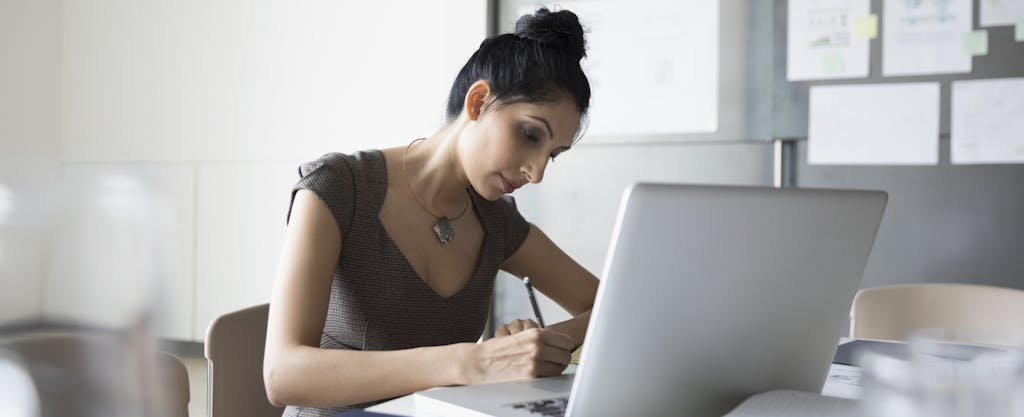 Businesswoman taking notes at laptop, preparing for meeting in conference room