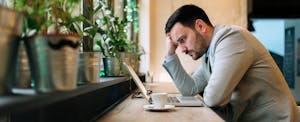 Worried man looking at laptop screen while sitting in coffee shop