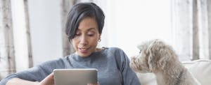 Woman sitting on her couch with her dog, reading on her tablet