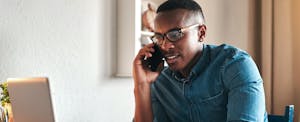 Young man at home on cellphone, contacting a credit bureau to get a copy of his credit report