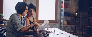 Two women sitting together on their bed, reading over their notes and using the rule of 72 to calculate their savings growth