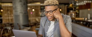 Man with glasses in a cafe, looking up no-fee checking on his laptop