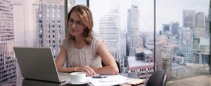 Woman working on computer with cityscape in background