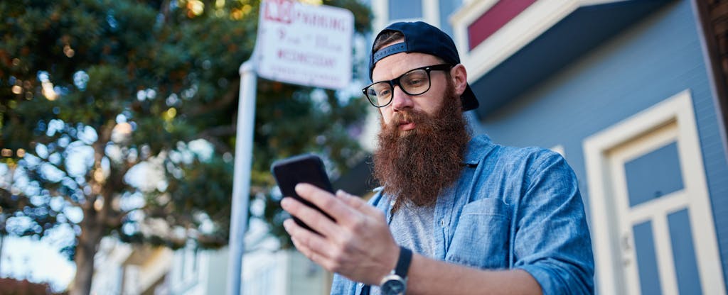 Man standing on the street, reading on his phone about apps like Branch