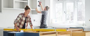 Builders install cabinetry in a brightly lit kitchen.