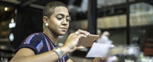 Young woman sitting outside at a cafe, concentrating as she deposits a check on her phone