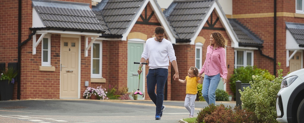 A mother and father hold the hands of their toddler as they walk past brick houses in their neighborhood where they pay HOA fees.