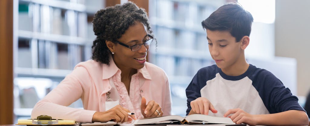 A tutor and a student in the campus library look at a textbook together.