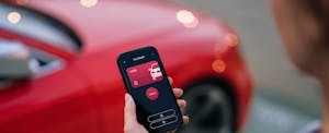 Over the shoulder view of a person looking at a car app on phone next to red car.